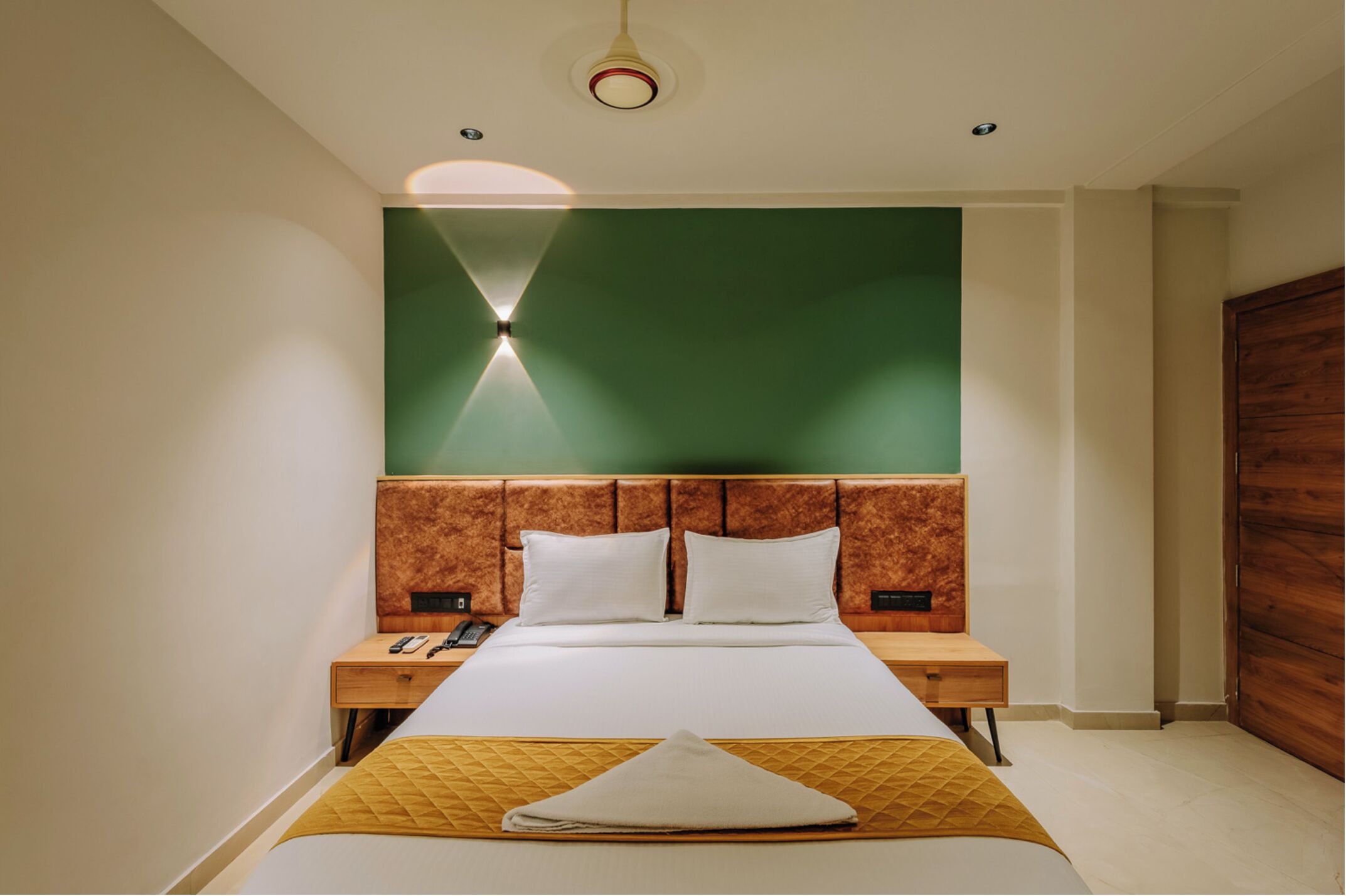 Una habitación de hotel moderna con una cama grande, cabecera de madera y una pared de acento verde.