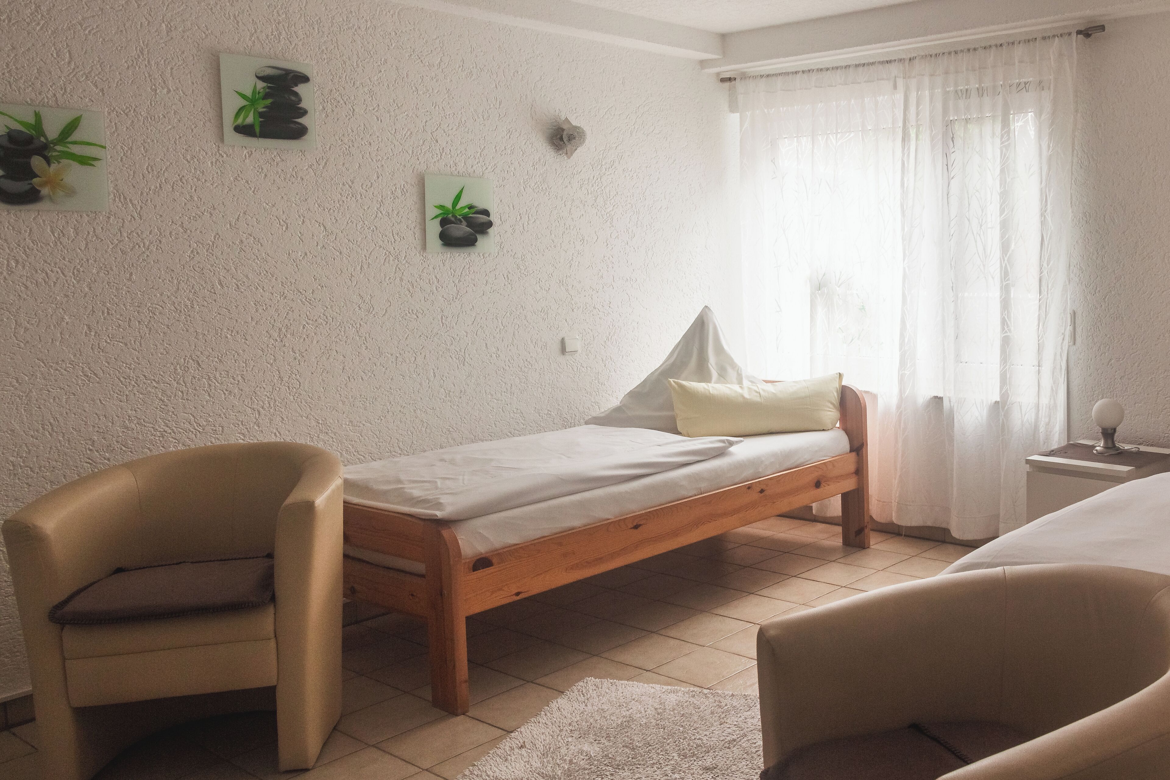 Ein kleines, gemütliches Zimmer mit einem Bett, einem Sessel und einem Nachttisch.