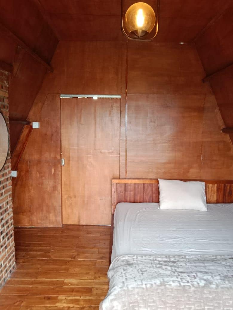 A cozy attic bedroom with a wooden ceiling, a single bed, and a hanging light fixture.