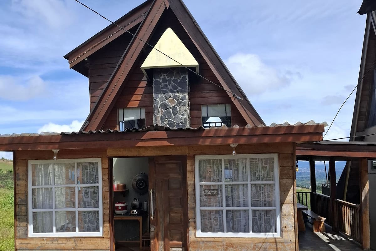 A wooden cabin with a stone fireplace, large windows, and a stone-tiled entrance.