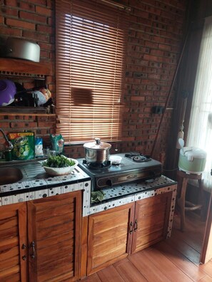 Una cocina con pared de ladrillo, armarios de madera, estufa y ventana con persianas.