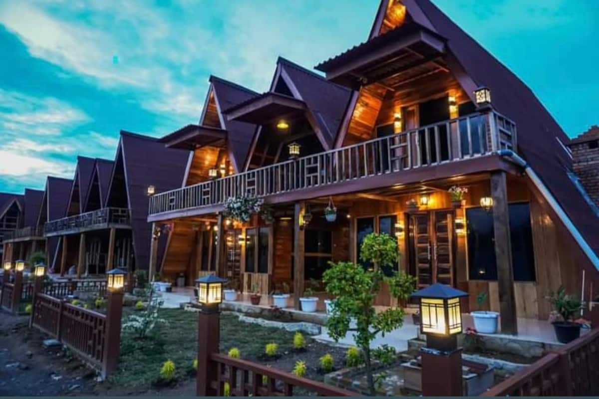 A row of wooden cabins with sloped roofs and balconies, surrounded by a landscaped garden with potted plants and a small pond.