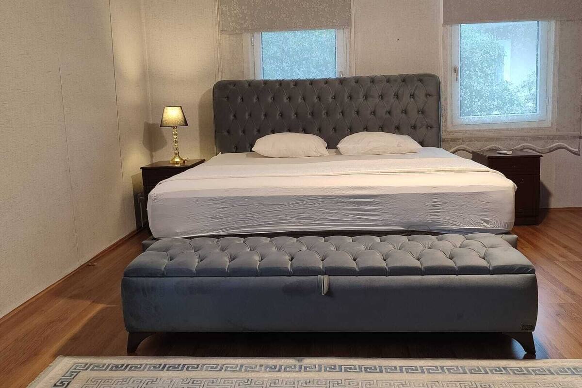A bedroom with a large bed, a bedside table with a lamp, and a window.