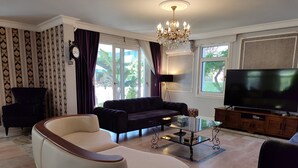 Un salon comprenant un canapé, un fauteuil, une table basse, un téléviseur et un lustre.