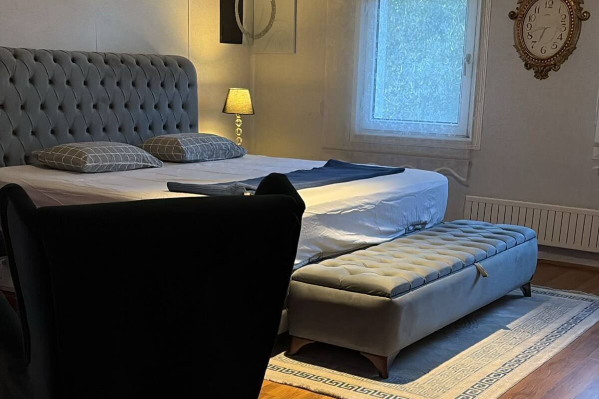 A bedroom with a bed, a chair, a lamp, a clock, and a window.
