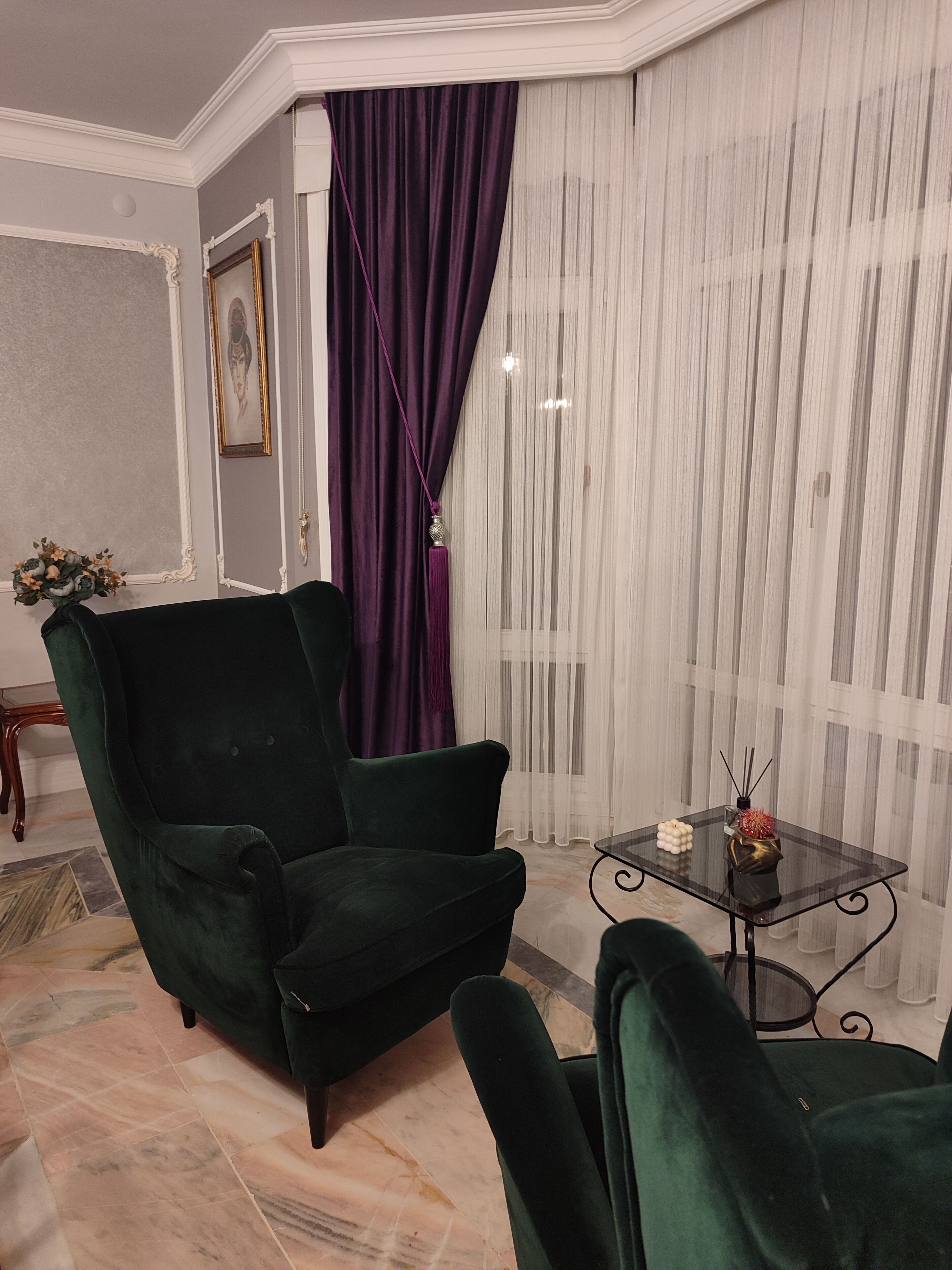 A room with a dark green armchair, a matching sofa, a glass coffee table, and a patterned floor.