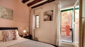 A bedroom with a large bed, a nightstand, a wall-mounted lamp, a window with curtains, and a view of an outdoor brick wall. - I Quattro Mori by Wonderful Italy (Venice)