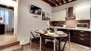 A modern kitchen with dark cabinetry, a flat-screen TV, and a dining area with a table set for two. - I Quattro Mori by Wonderful Italy (Venice)