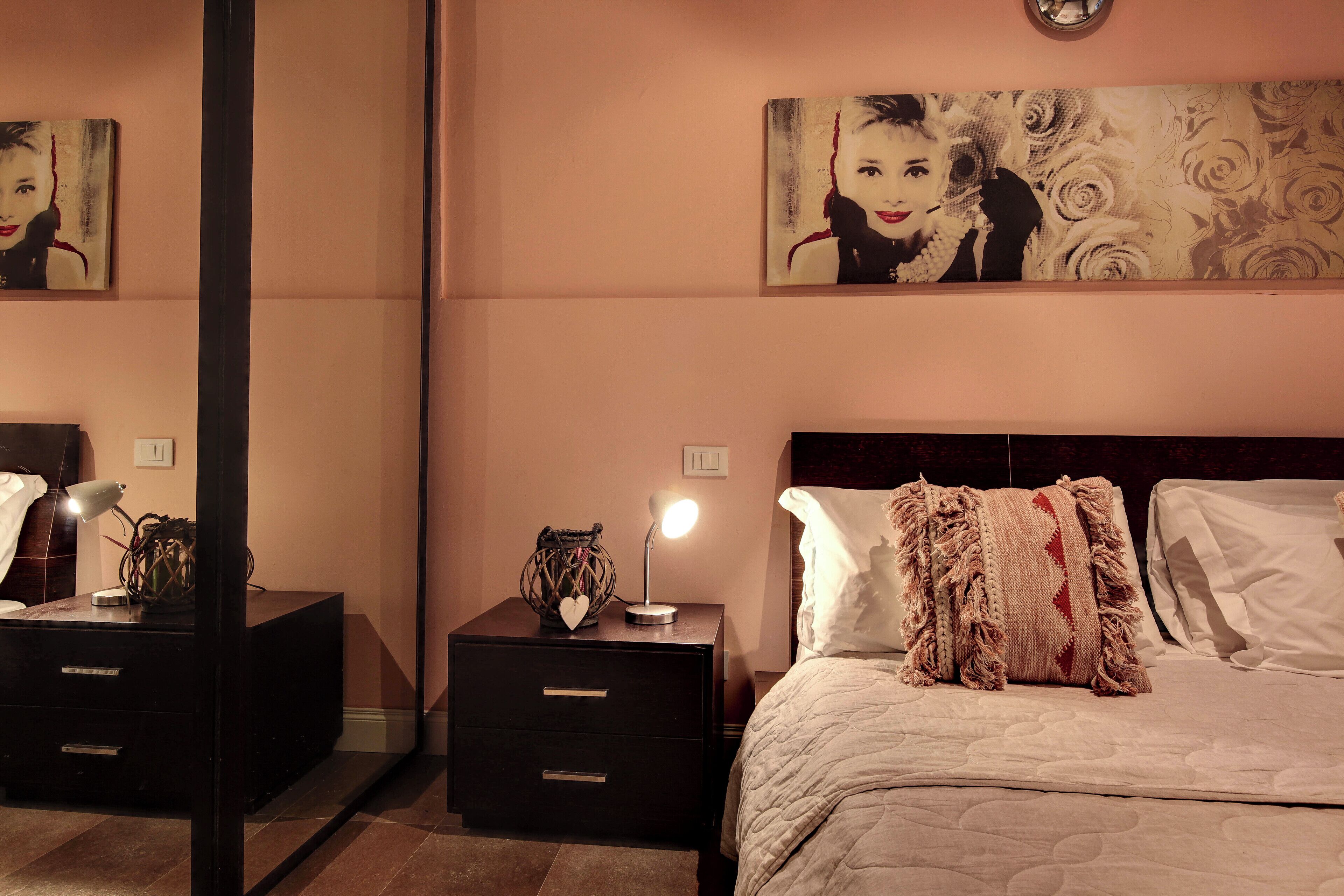 A bedroom with a bed, bedside tables, a nightstand, and a wall-mounted lamp.
