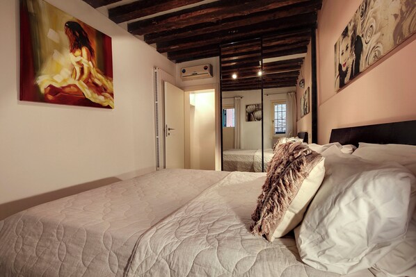 Un dormitorio con una cama grande, un cuadro en la pared y un techo con vigas a la vista.
