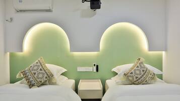 A hotel room with two beds, a bedside table, a nightstand, a wall-mounted air conditioner, and a wall-mounted projector.