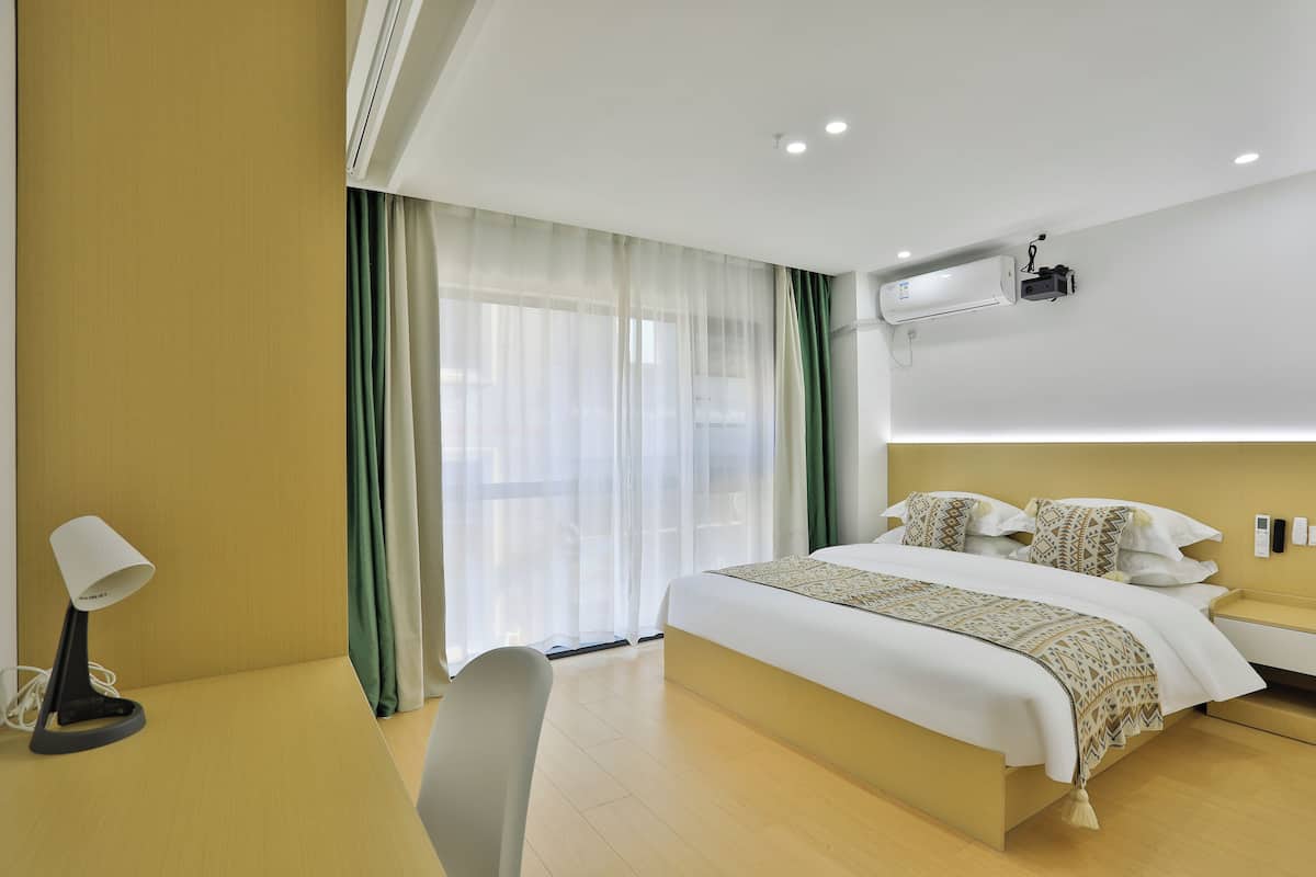 A hotel room with a bed, bedside table, lamp, and curtains.