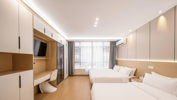 Une chambre d’hôtel moderne équipée de deux lits, d’un bureau, d’une télévision et d’une grande fenêtre avec des rideaux.