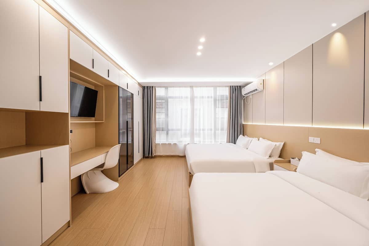 A modern hotel room with two beds, a desk, a TV, and a large window with curtains.