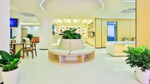Un hall d’entrée moderne et bien éclairé, doté d’un espace salon circulaire, d’un comptoir de réception et d’une plante au centre.