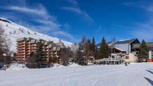 Ein verschneites Skigebiet mit einem großen Gebäudekomplex, Skipfällen und blauem Himmel.