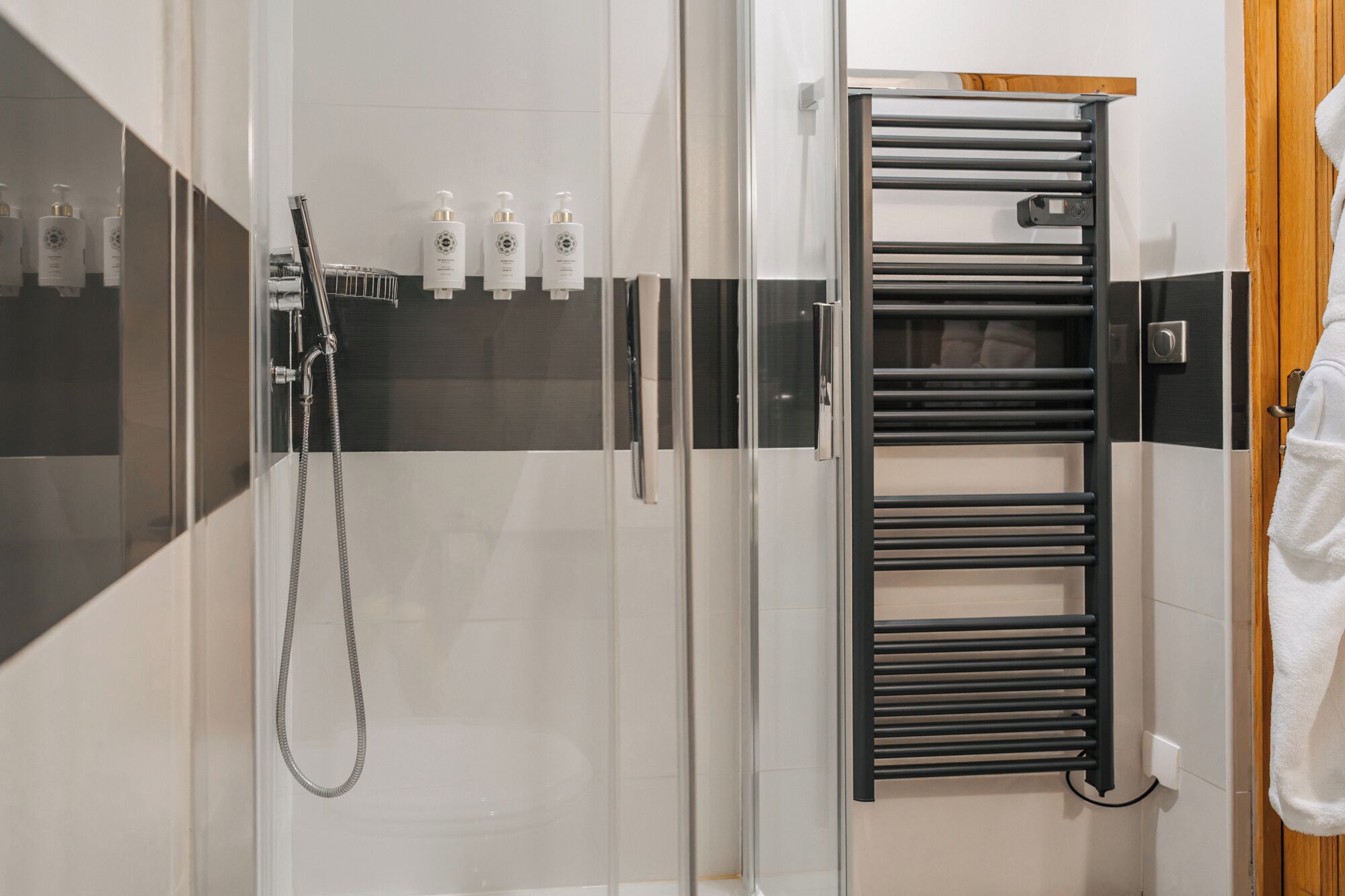 A modern bathroom with a glass shower enclosure, a black towel rack, and toiletries on the wall.