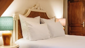 Una cama bien hecha con sábanas y almohadas blancas, una puerta de madera y dos lámparas de noche con pantallas estampadas.