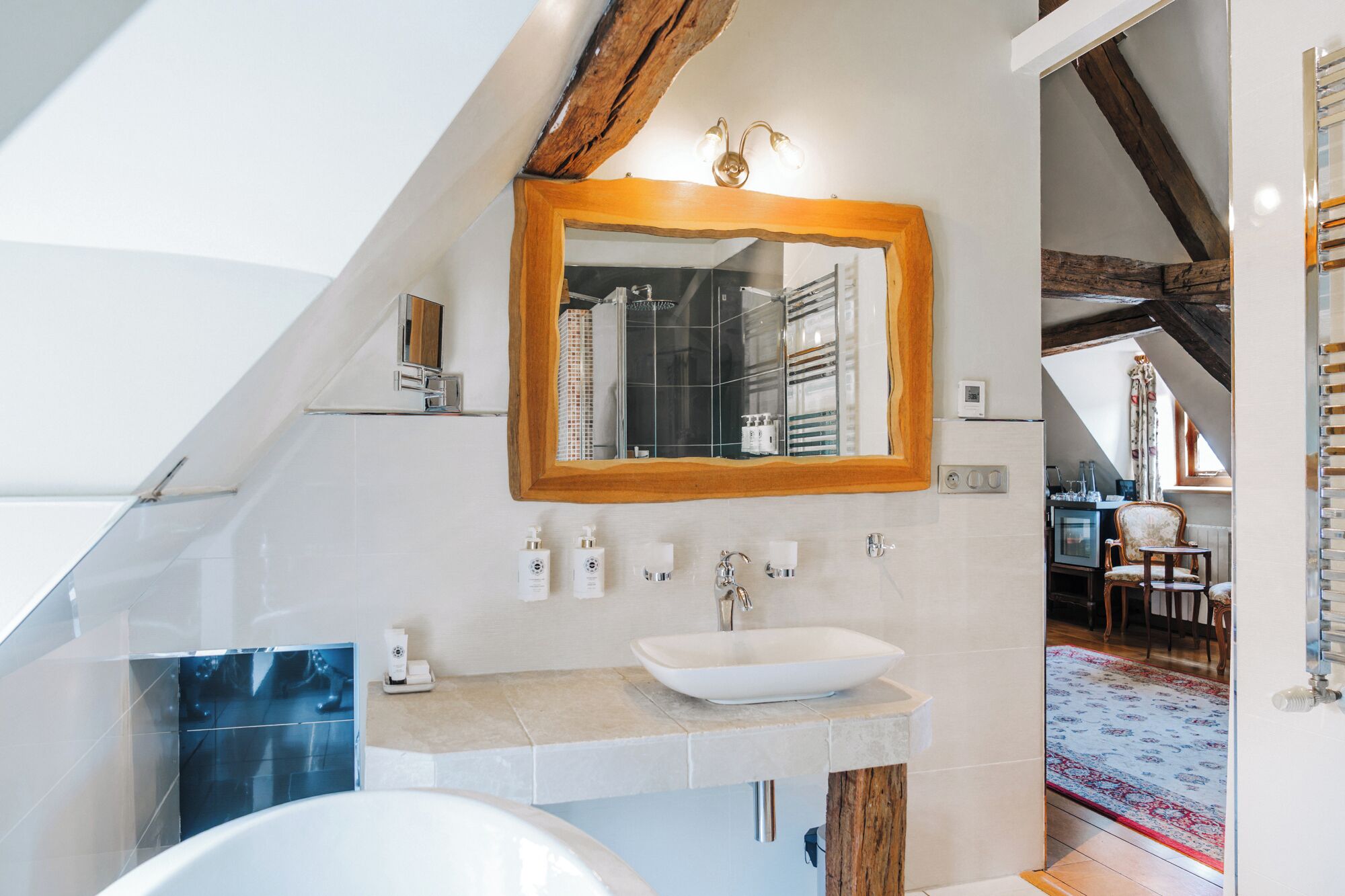 Une salle de bain moderne avec un plafond en pente, un grand miroir, un lavabo blanc et une baignoire.
