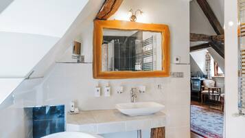 A modern bathroom with a sloped ceiling, a large mirror, a white sink, and a bathtub.