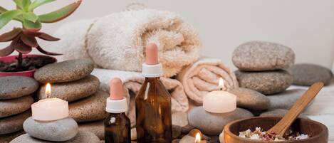 Un ambiente de spa con velas, piedras, un cuenco de madera con hierbas y una planta en maceta.