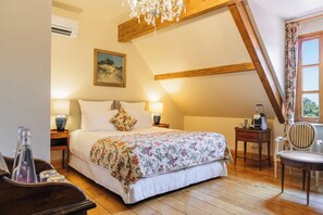 Un dormitorio con techo de madera, una cama con ropa de cama floral, un cuadro en la pared y una ventana con cortinas.