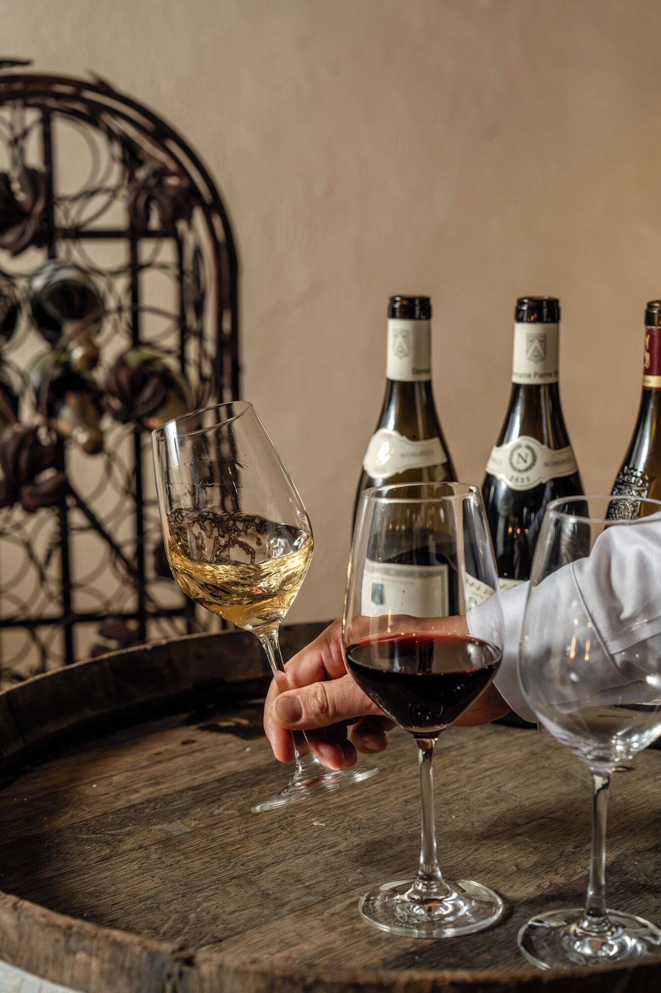 Un plateau en bois avec deux verres à vin, l’un rempli de vin blanc et l’autre de vin rouge, et deux bouteilles de vin en arrière-plan.