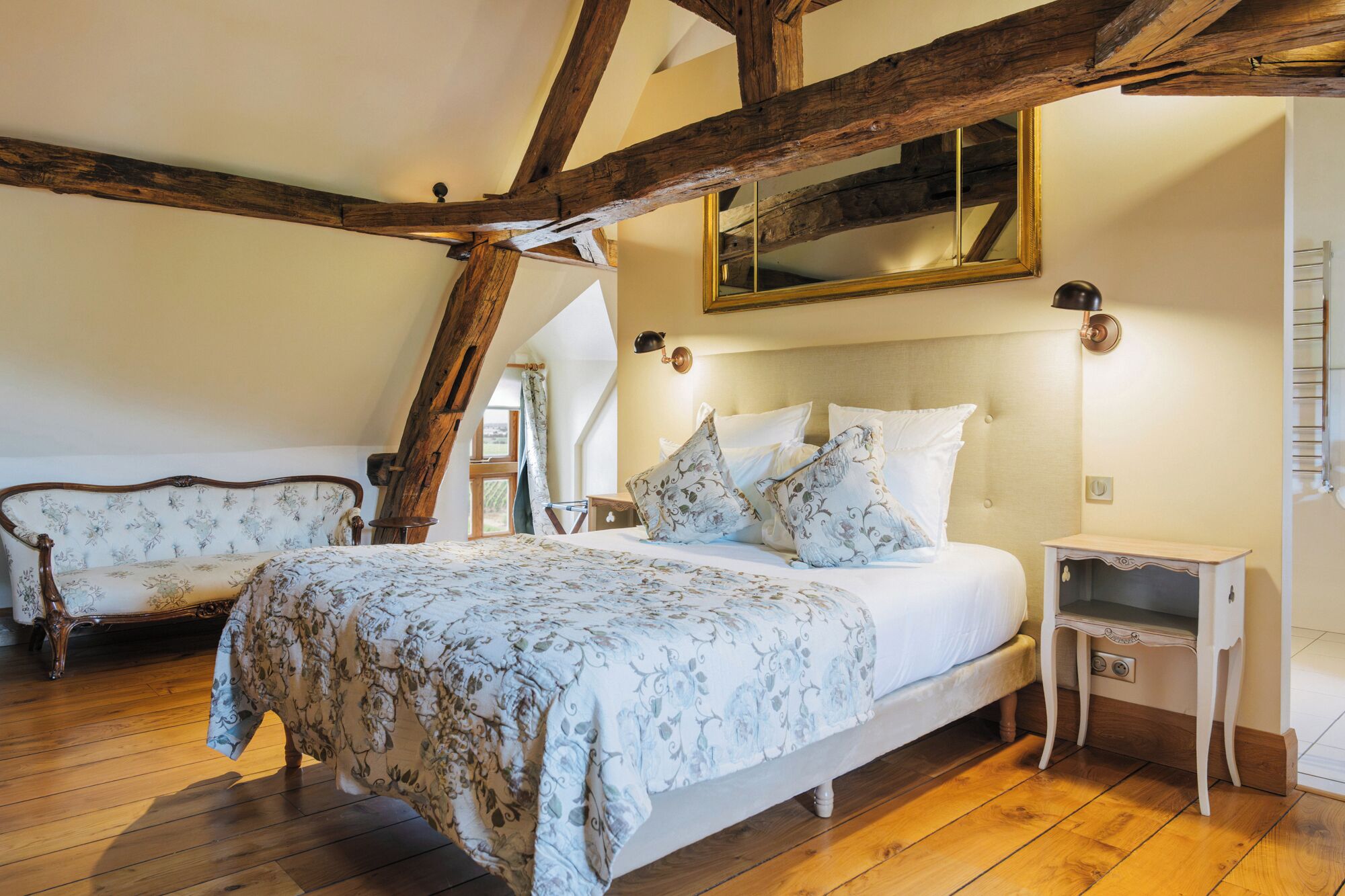 Une chambre à coucher avec un lit, une table de chevet, un miroir et une poutre en bois au plafond.