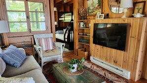 A cozy cabin interior with a wooden interior, a sofa, a chair, a television, and a small table with a plant. - Private lake cabin. WiFi, Beach, Pontoon Rental. Booking for summer of 27! (Nevis)