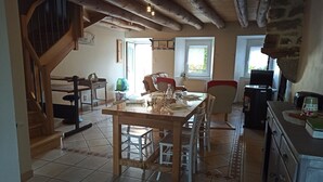 A dining area with a wooden table and chairs, a staircase, and a stone wall. - Quiet country house  (Le Buisson)