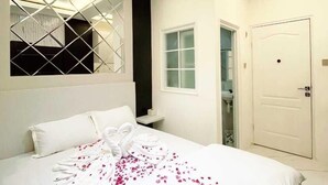 A hotel room with a bed, a window with a geometric design, a door, and a small table with a bottle. - Rafithahotel (Baturetno)