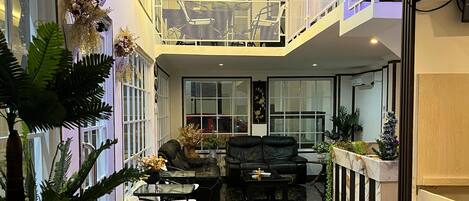Un espacio interior amplio con suelo de mármol negro, una zona de estar con sofá y sillones, y un balcón con barandilla.