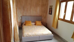 A bedroom with a bed, curtains, a window, and a painting on the wall.