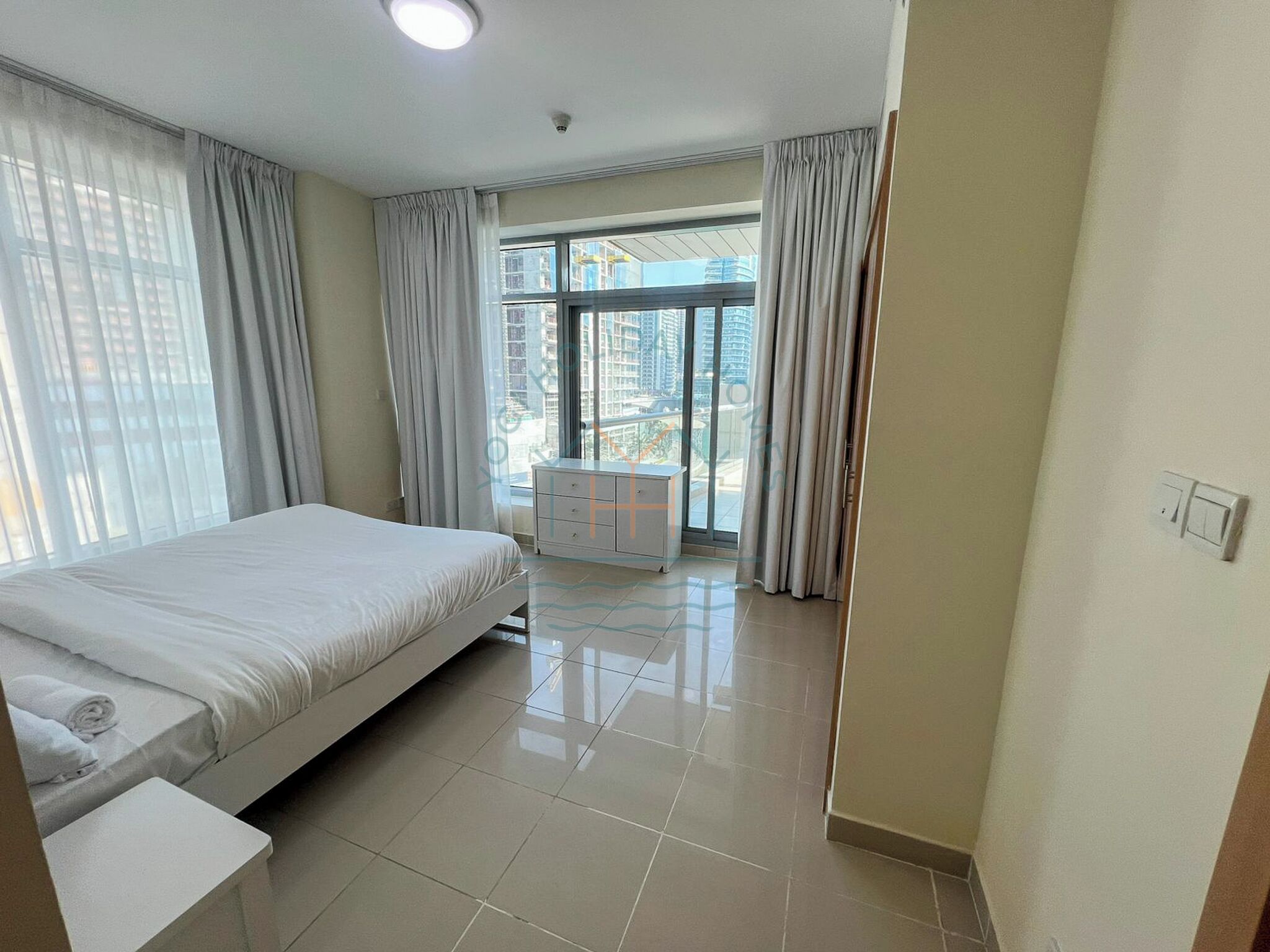 A modern hotel room with a large bed, a dresser, and a balcony with a city view.