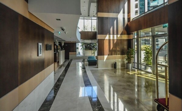 A modern hotel lobby with a marble floor, wooden paneling, and large windows offering views of the outside.