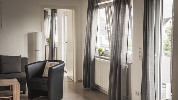 A modern living room with a sofa, a black armchair, and a wooden coffee table. There is a window with curtains and a view of the outside. - Vacation apartment I Waldstraße - ideal for up to 4 people (Alsbach-Hähnlein)