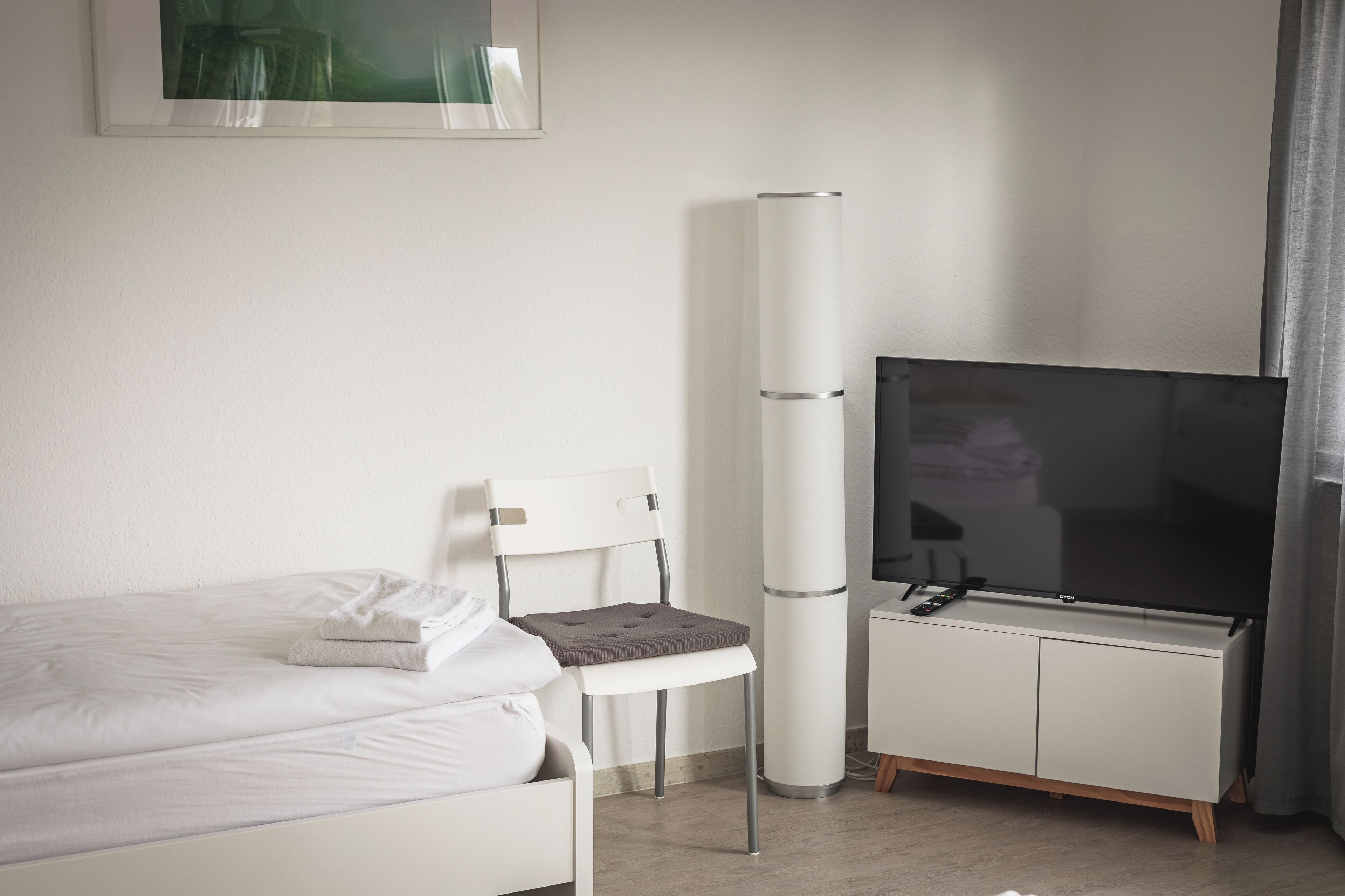 A hotel room with a bed, a chair, a TV on a cabinet, and a large window.