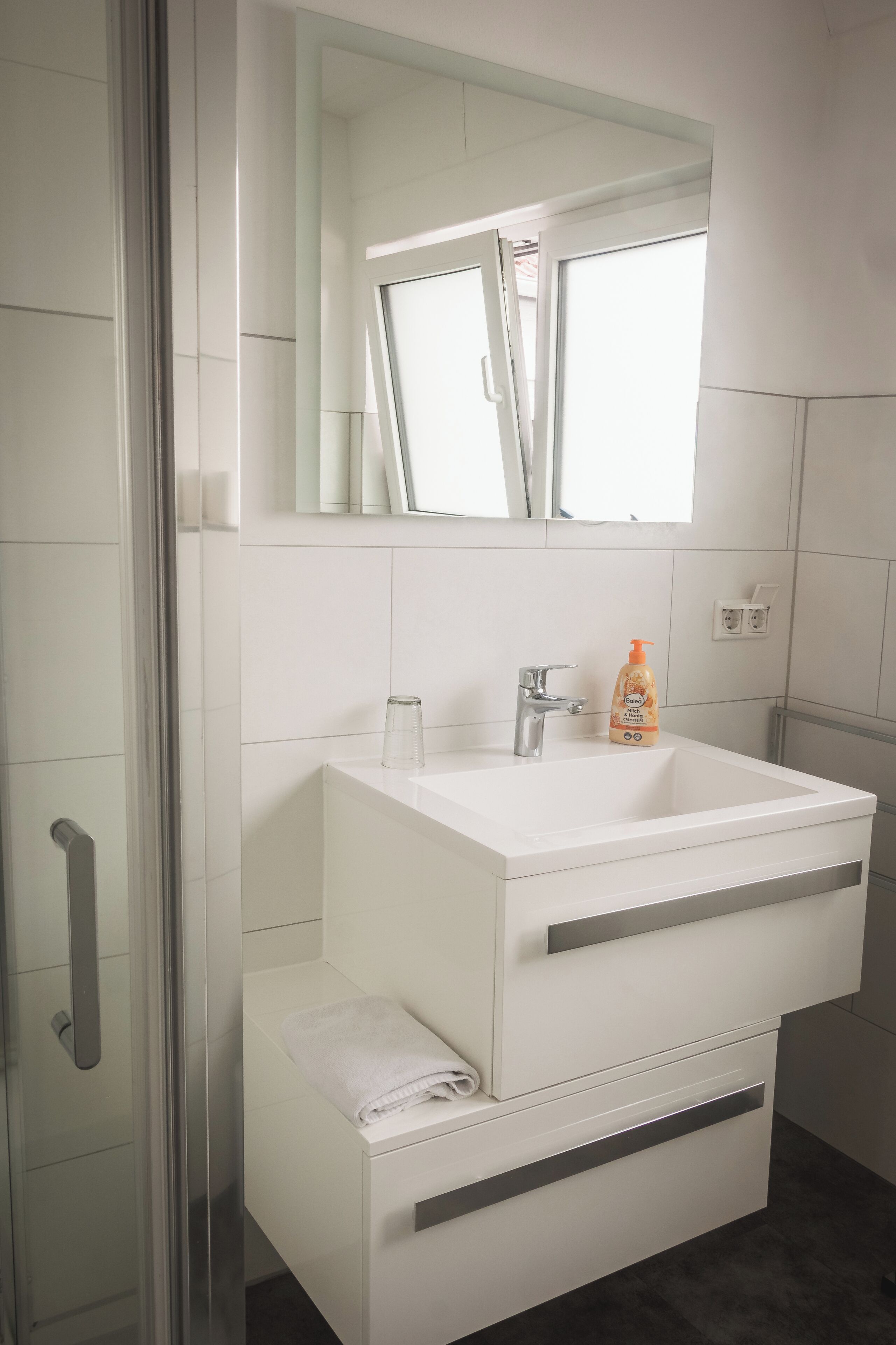A modern bathroom with a white sink, a glass shower enclosure, and a mirror above the sink.