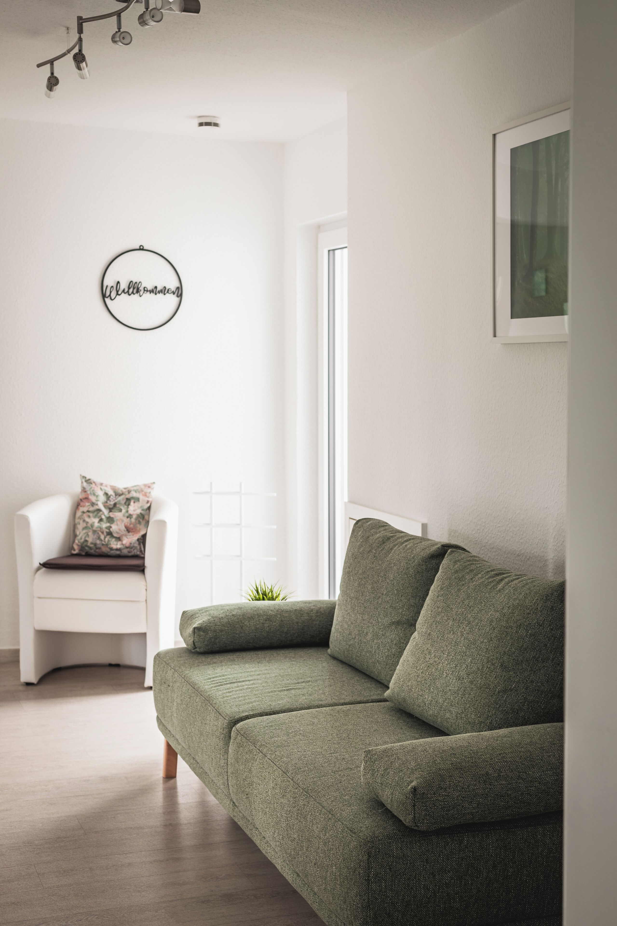 A modern living room with a green sofa, a white armchair, and a small plant.