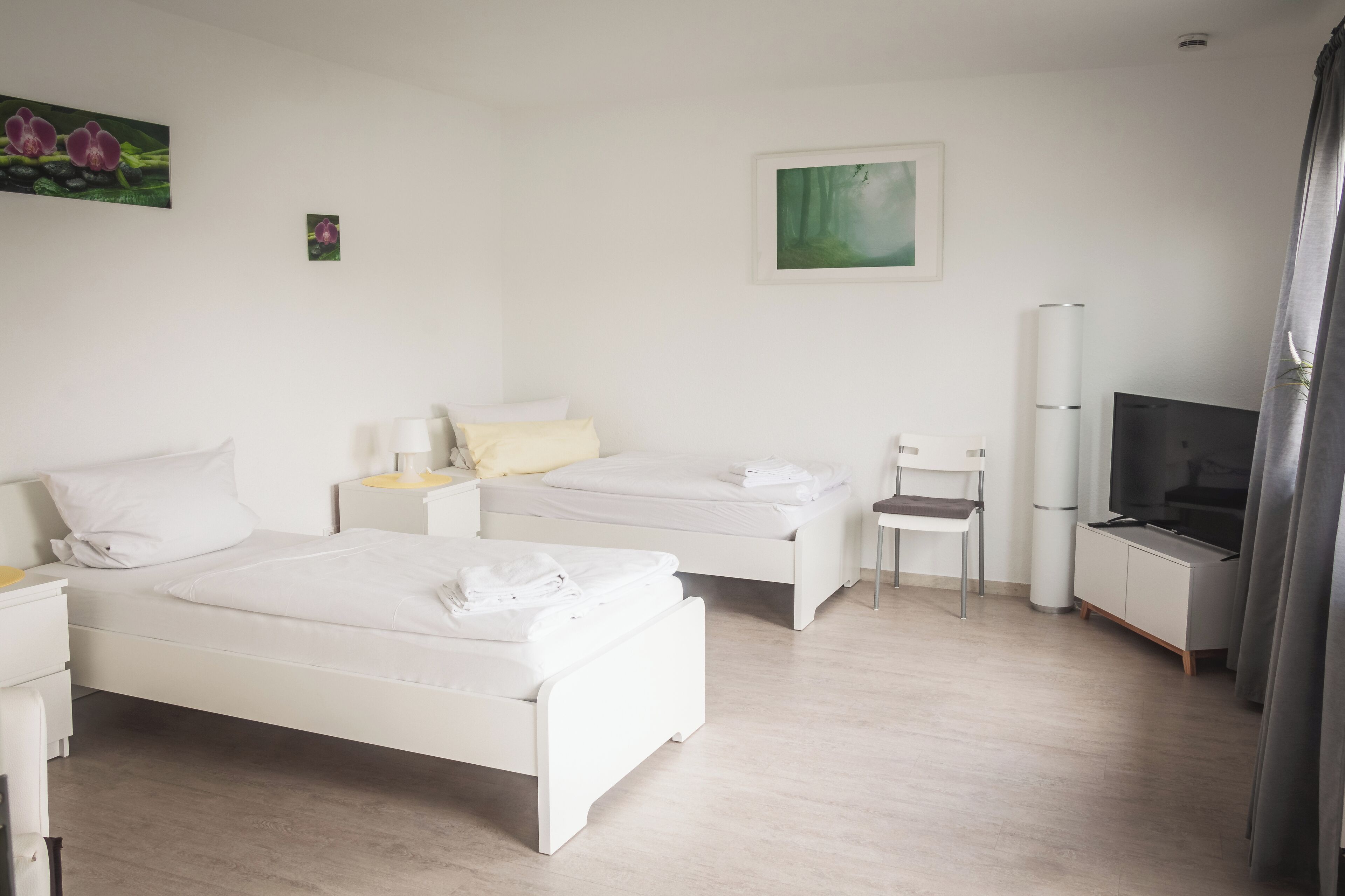 Et moderne hotelværelse med to enkeltsenge, et lille skrivebord, en stol, et fjernsyn og et skab.
