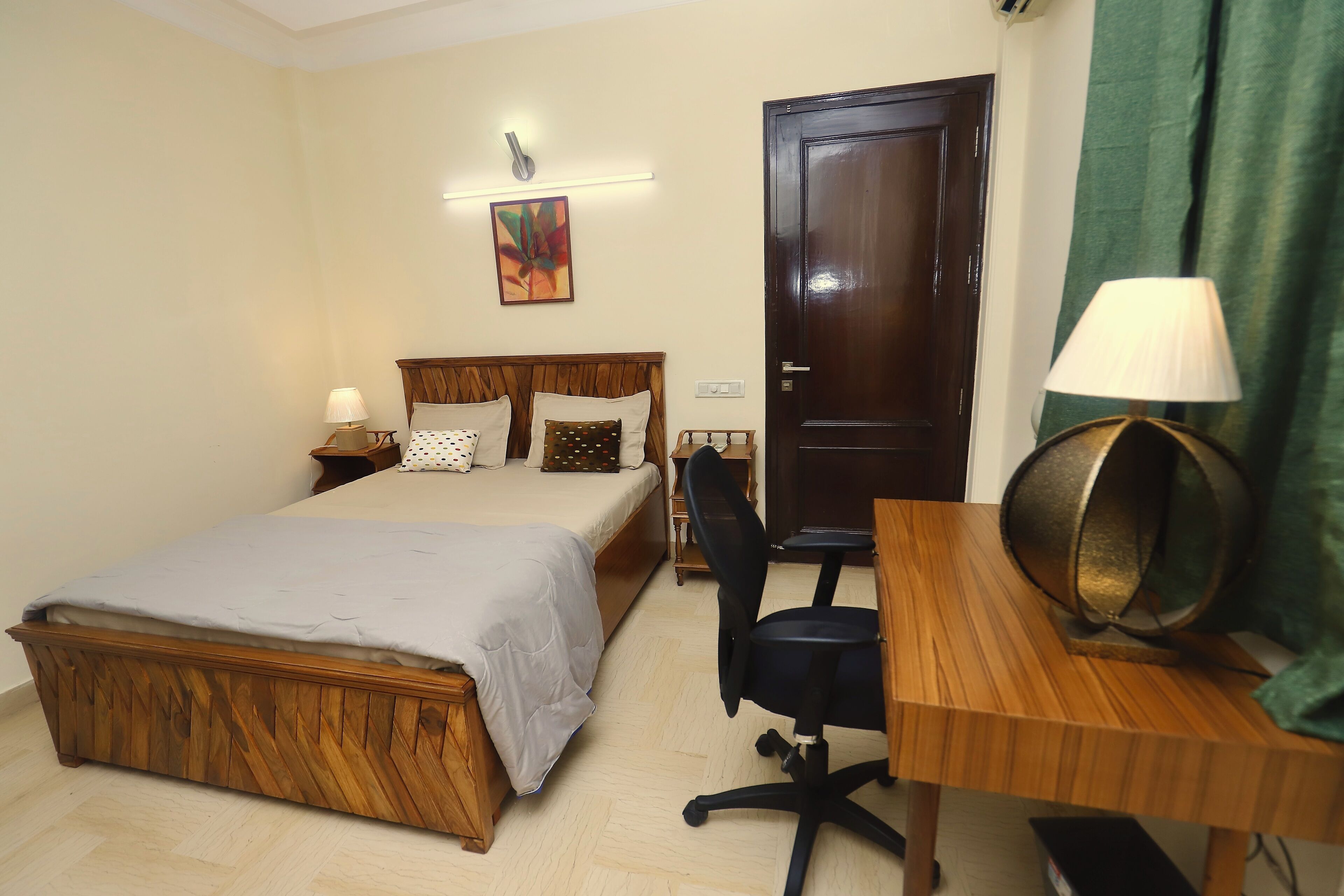 A bedroom with a wooden bed, a desk, a chair, a lamp, and a door.