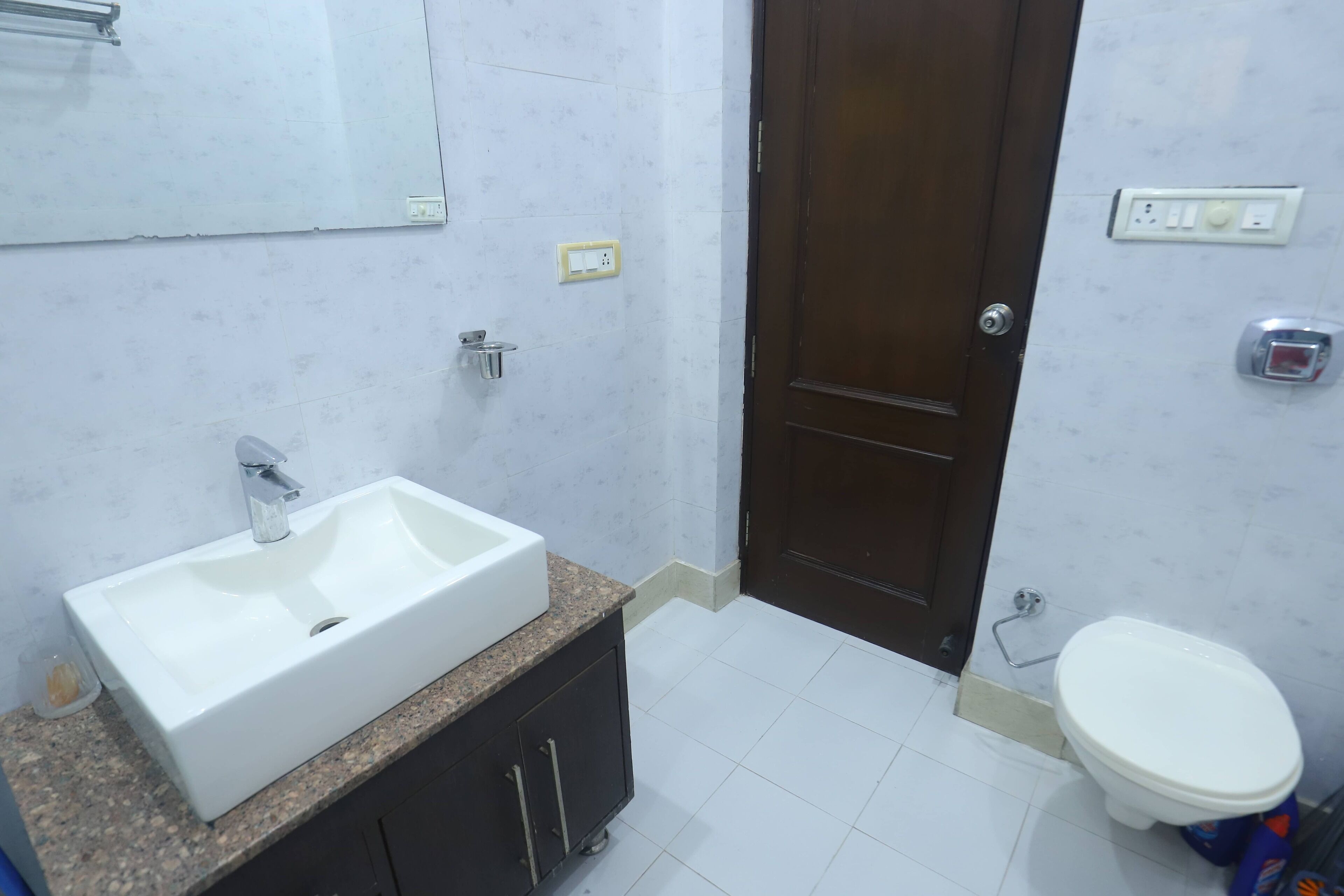 Un bagno con un lavandino bianco, mobiletti scuri, uno specchio, un water e una porta.