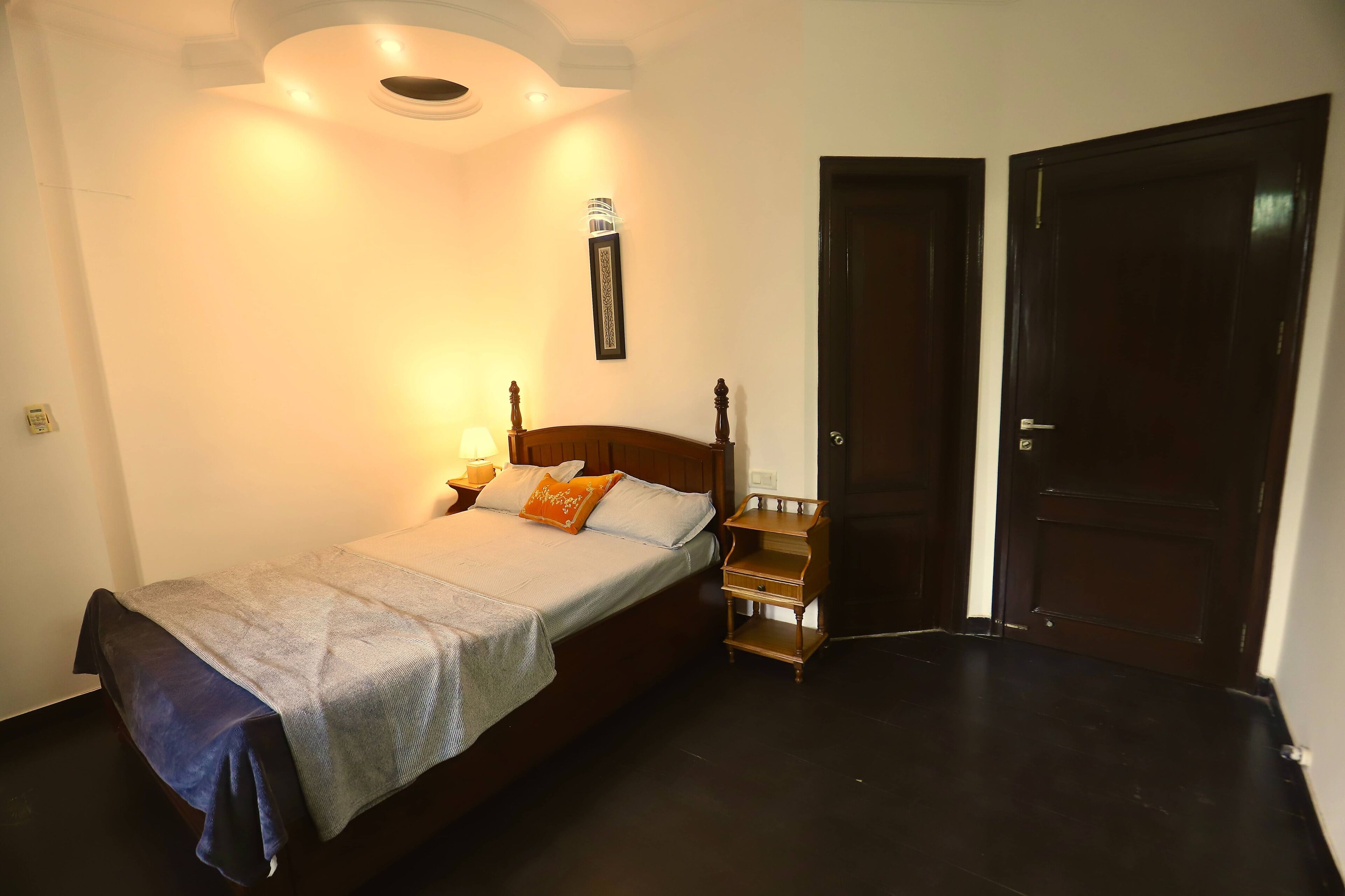 Un dormitorio con cama, mesitas de noche, una lámpara de pared y una puerta.