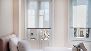 Quarto de hotel com cama, travesseiros, janela e vista para edifícios.