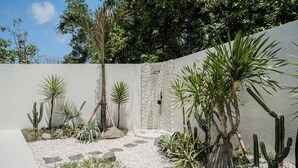 Een tuin met diverse cactussen en planten, een stenen muur en een witte hek.
