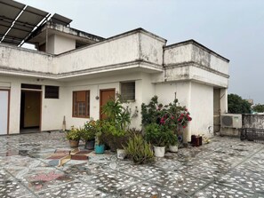 A building with a tiled courtyard, potted plants, and a visible door. - Raghav Vilas (Varanasi)