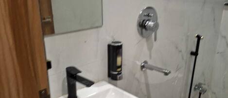 A bathroom with a white sink, a mirror, a handheld showerhead, and a toilet.