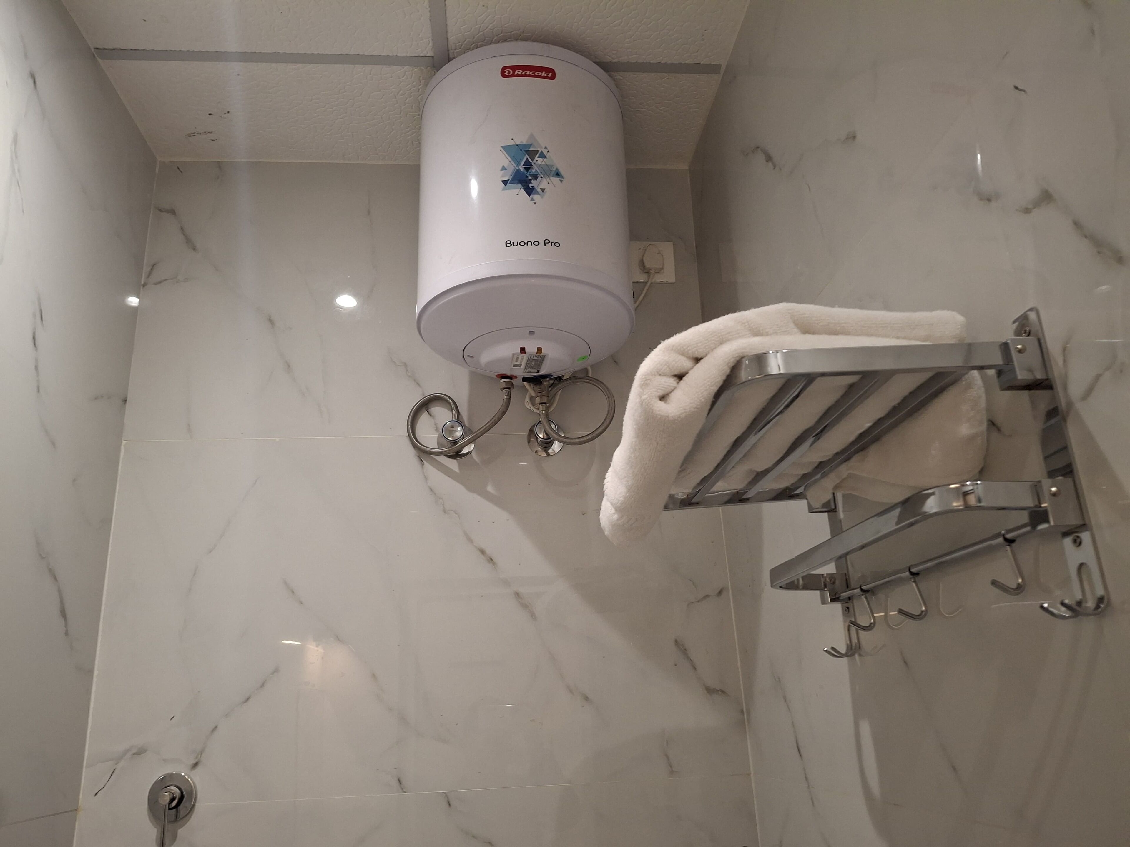 Un baño con piso de mármol blanco, un perchero con una toalla doblada y un secador de manos en la pared.