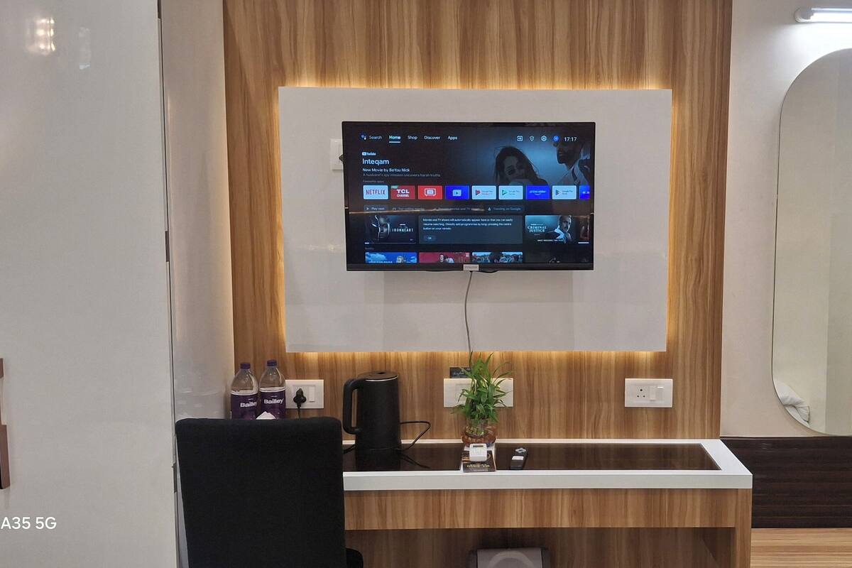 Moderni huone, jossa on seinälle asennettu televisio, josta näkyy suoratoistopalvelun käyttöliittymä, työpöytä, jossa on kahvinkeitin, ja peili.