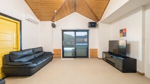 Een moderne woonkamer met een zwarte leren bank, een flatscreen-tv op een zwarte standaard, een gele deur en een schuifpui die leidt naar een balkon met uitzicht op een berg.